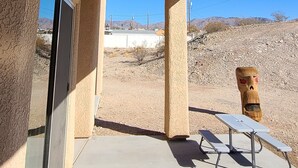 Un patio couvert avec un ventilateur de plafond, une table et des chaises, et une vue sur un paysage désertique.
