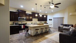 Une cuisine moderne avec des meubles de couleur bois foncé, un îlot central doté de tabourets, un ventilateur de plafond et un éclairage encastré.