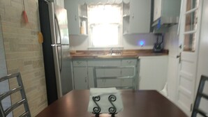 A dining table with chairs, a refrigerator, a sink, and cabinets in a kitchen area. - Mid Century Modern McKenzie (McKenzie)
