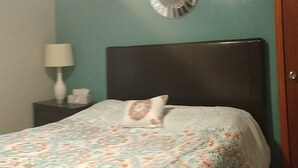 A bed with a patterned bedspread, a bedside lamp, and a mirror on the wall. - Mid Century Modern McKenzie (McKenzie)