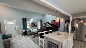 A modern kitchen with a built-in island, a dining area with a sofa and chairs, and a living room with a piano.