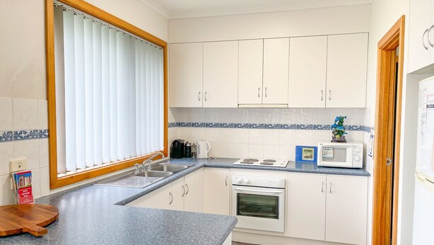 A compact kitchen with white cabinets, a granite countertop, a built-in oven, and a microwave. - Dolphin Court - Park your car and walk to all that Robe has to offer (Robe)