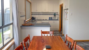 A compact kitchen with white cabinets, a wooden dining table, and a small island. - Dolphin Court - Park your car and walk to all that Robe has to offer (Robe)