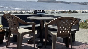 A wooden deck with a round table and four chairs, overlooking a rocky shoreline with a lighthouse in the distance. - The Ebb Tide Beach Bungalow (Half Moon Bay)