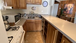 A compact kitchen with wooden cabinets, a microwave, a stove, and a sink. - The Ebb Tide Beach Bungalow (Half Moon Bay)