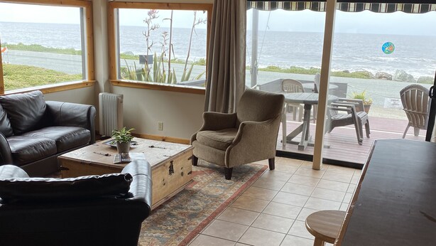 A cozy living room with a view of the ocean, furnished with a sofa, armchair, and coffee table. - The Ebb Tide Beach Bungalow (Half Moon Bay)