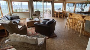 A spacious living area with a view of the sea, featuring wicker furniture, a bar area, and a large sliding glass door. - The Ebb Tide Beach Bungalow (Half Moon Bay)