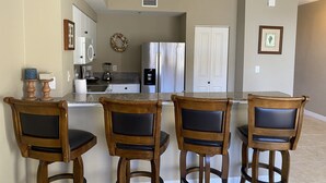 Una cocina con una isla central, cuatro taburetes de madera, un refrigerador, un lavamanos y puertas dobles.