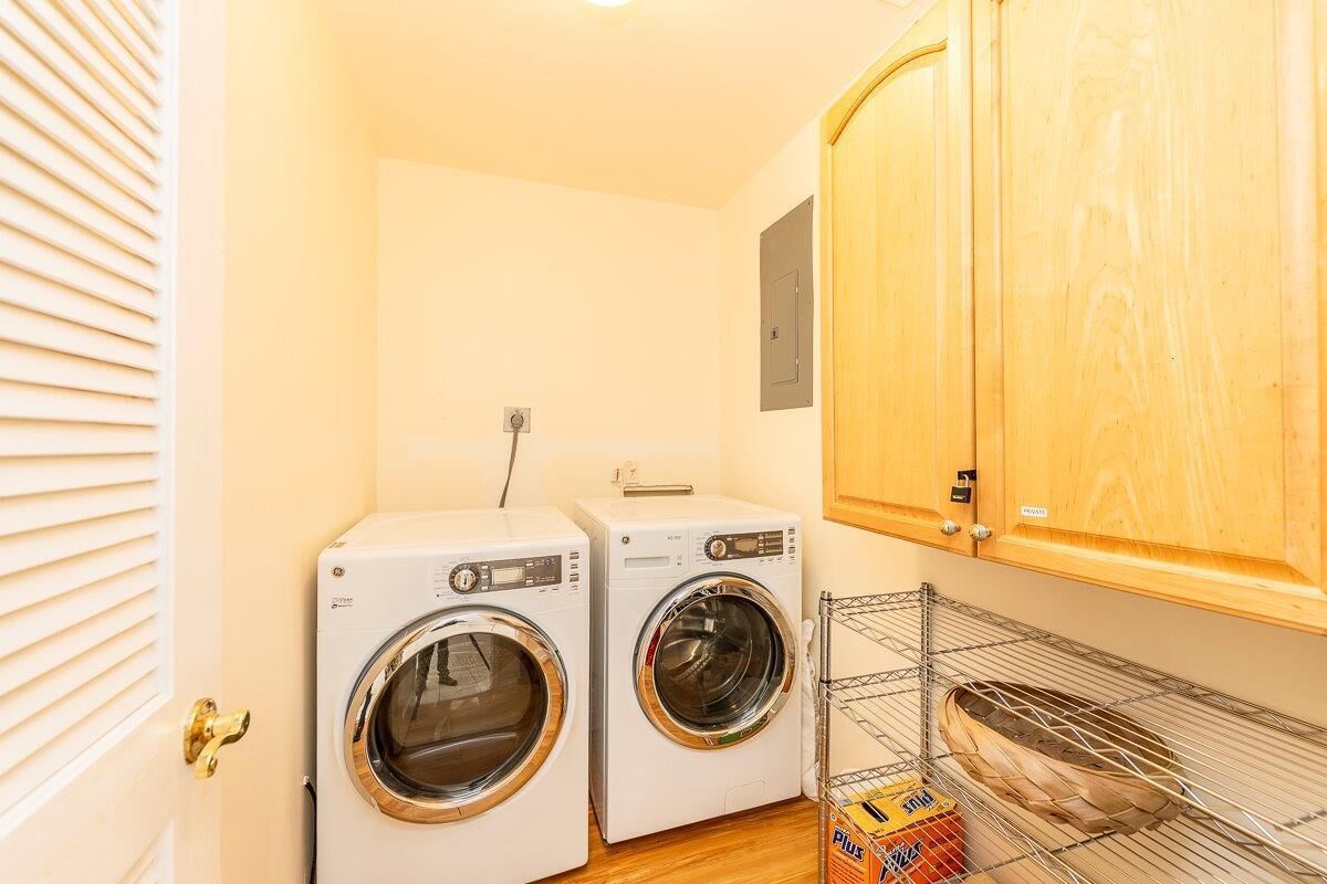 A laundry room with two front-loading washing machines, a metal shelf with a basket, and wooden cabinets.
