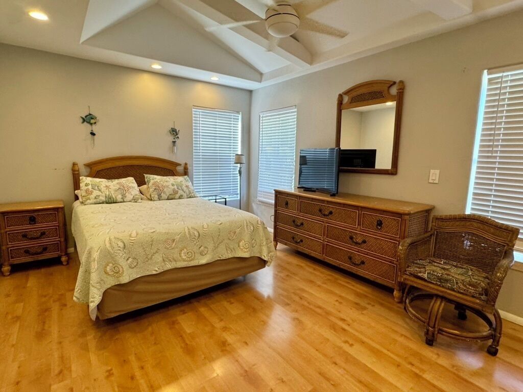 A bedroom with a wooden bed, dresser, and chair, a ceiling fan, and a large mirror.