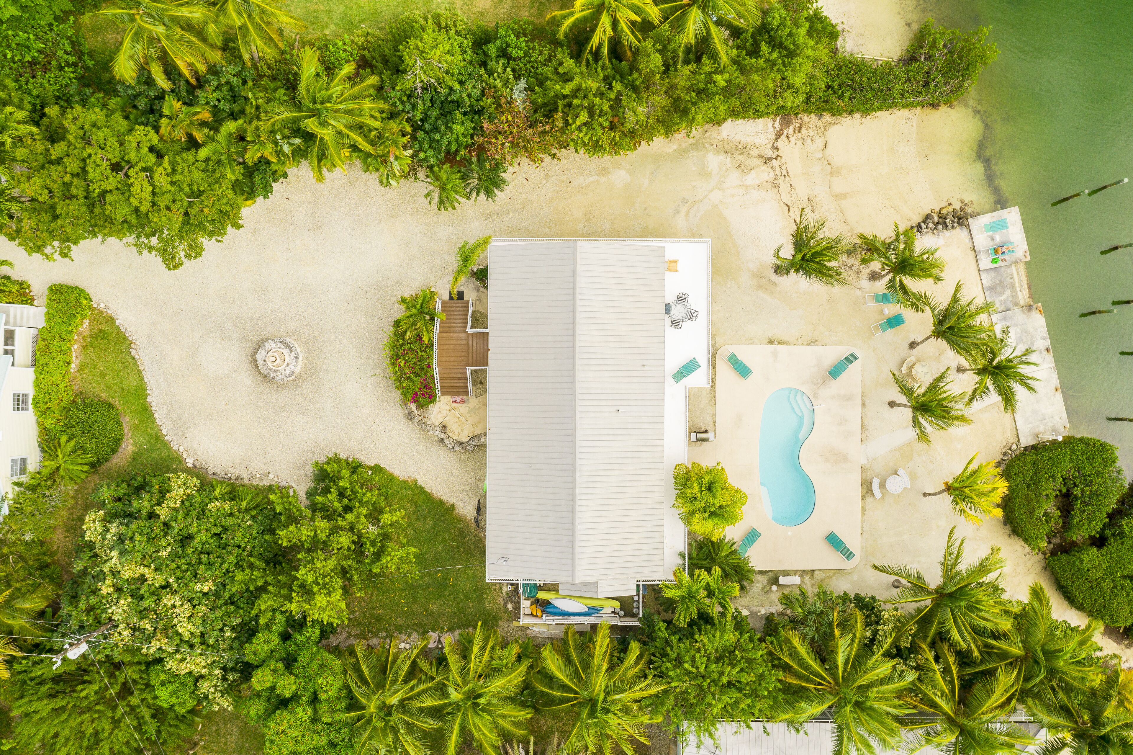 Vue aérienne d’une propriété située en bord de mer, avec une piscine, des chaises longues et un petit bâtiment doté d’un toit.