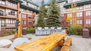 A courtyard with a wooden table and benches, a large tree, and a building with balconies.