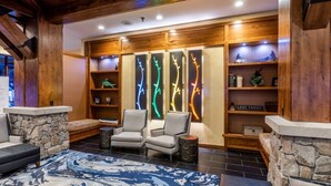 A lobby with stone walls, two armchairs, a patterned rug, and illuminated tree branch decorations.