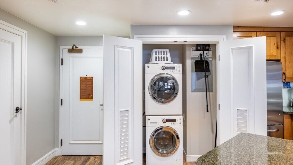 A laundry room with stacked washers and dryers, a wooden cabinet, and a countertop.