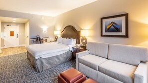 A hotel room with a bed, a sofa, a desk with a lamp, a framed picture on the wall, and a door leading to another room. - Lake Tahoe | Slopes & Village | Hot Tub | 2BR Villa (South Lake Tahoe)