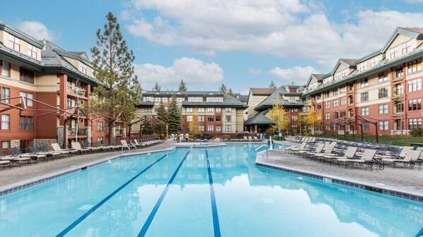 A swimming pool with lounge chairs, surrounded by multi-story buildings with balconies and a clear sky. - Lake Tahoe | Slopes & Village | Hot Tub | 2BR Villa (South Lake Tahoe)