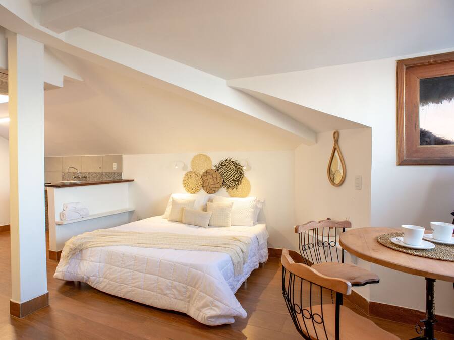 Een slaapkamer met een groot bed, een houten stoel, een tafeltje met kopjes en een wandklok.