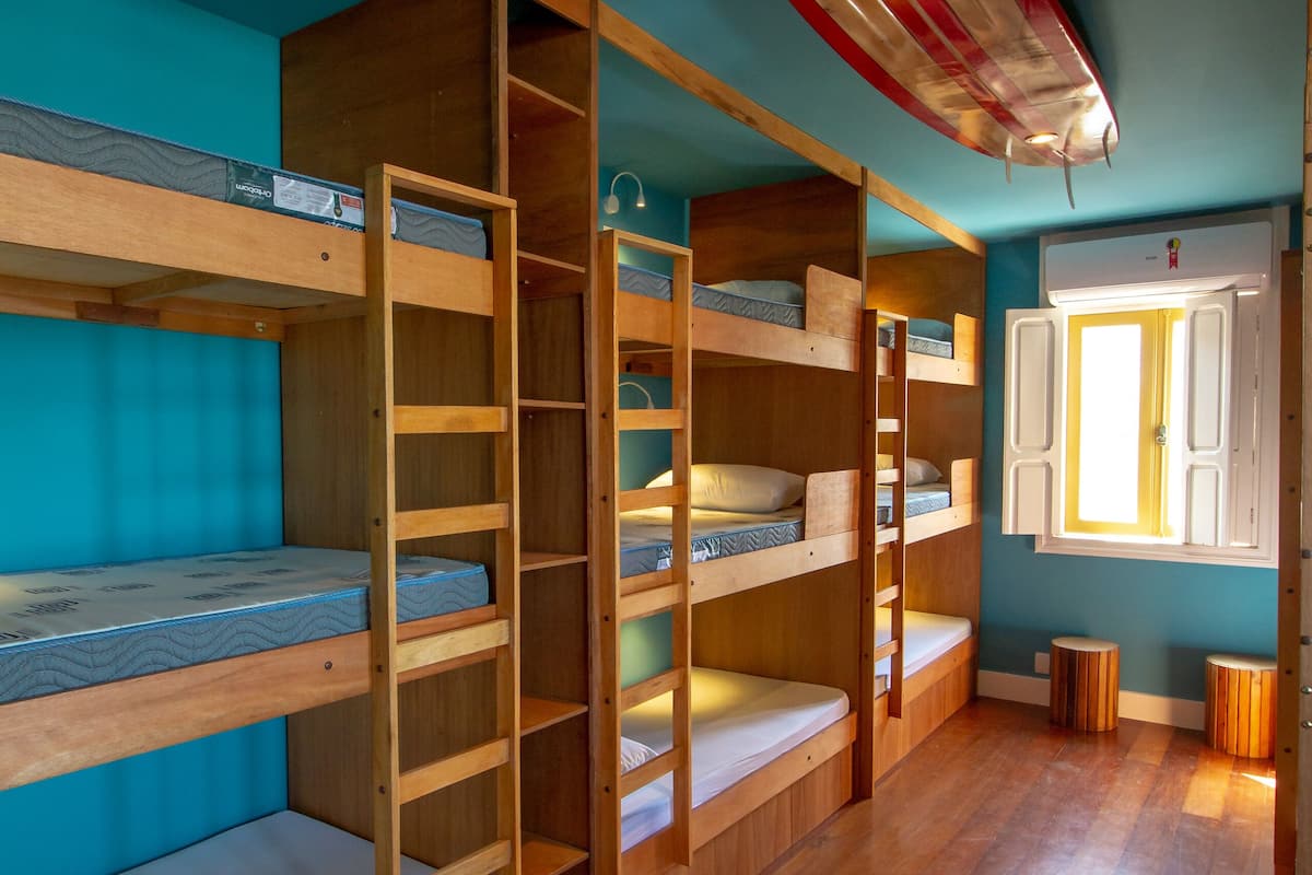 A room with bunk beds, a surfboard, and a window with shutters.
