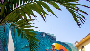 Zona de piscina al aire libre con un mural de escena submarina, sillas de descanso y una estructura de techo de paja.