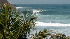 Vista costera con olas, un velero a lo lejos y una montaña al fondo.