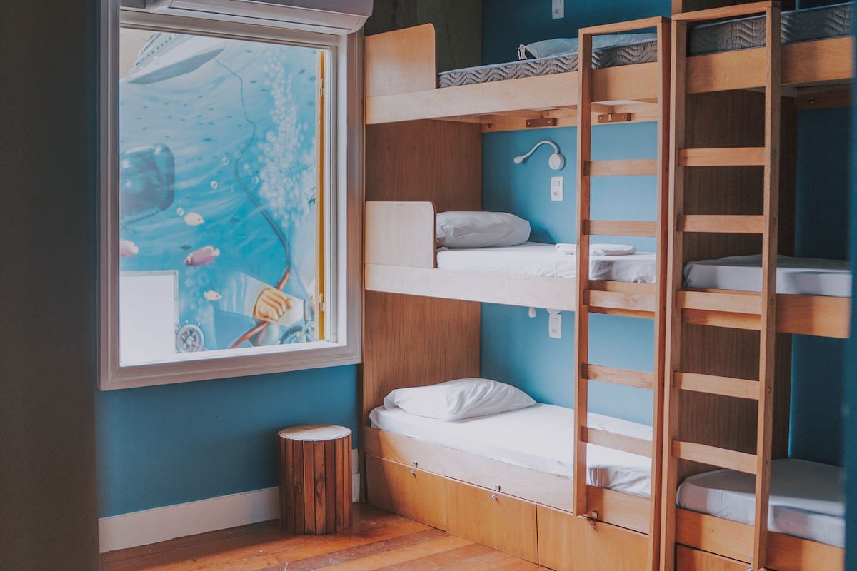 A compact room with bunk beds, a small window with a view of the sea, and a ceiling fan.