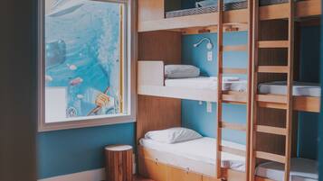 Une petite chambre avec des lits superposés, une petite fenêtre donnant sur la mer et un ventilateur de plafond.