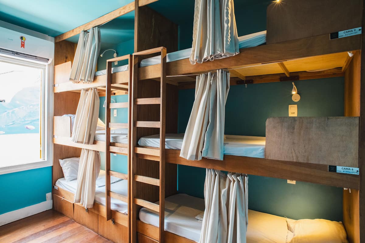 A bunk bed room with wooden bunk beds, a ladder, and a window with curtains.