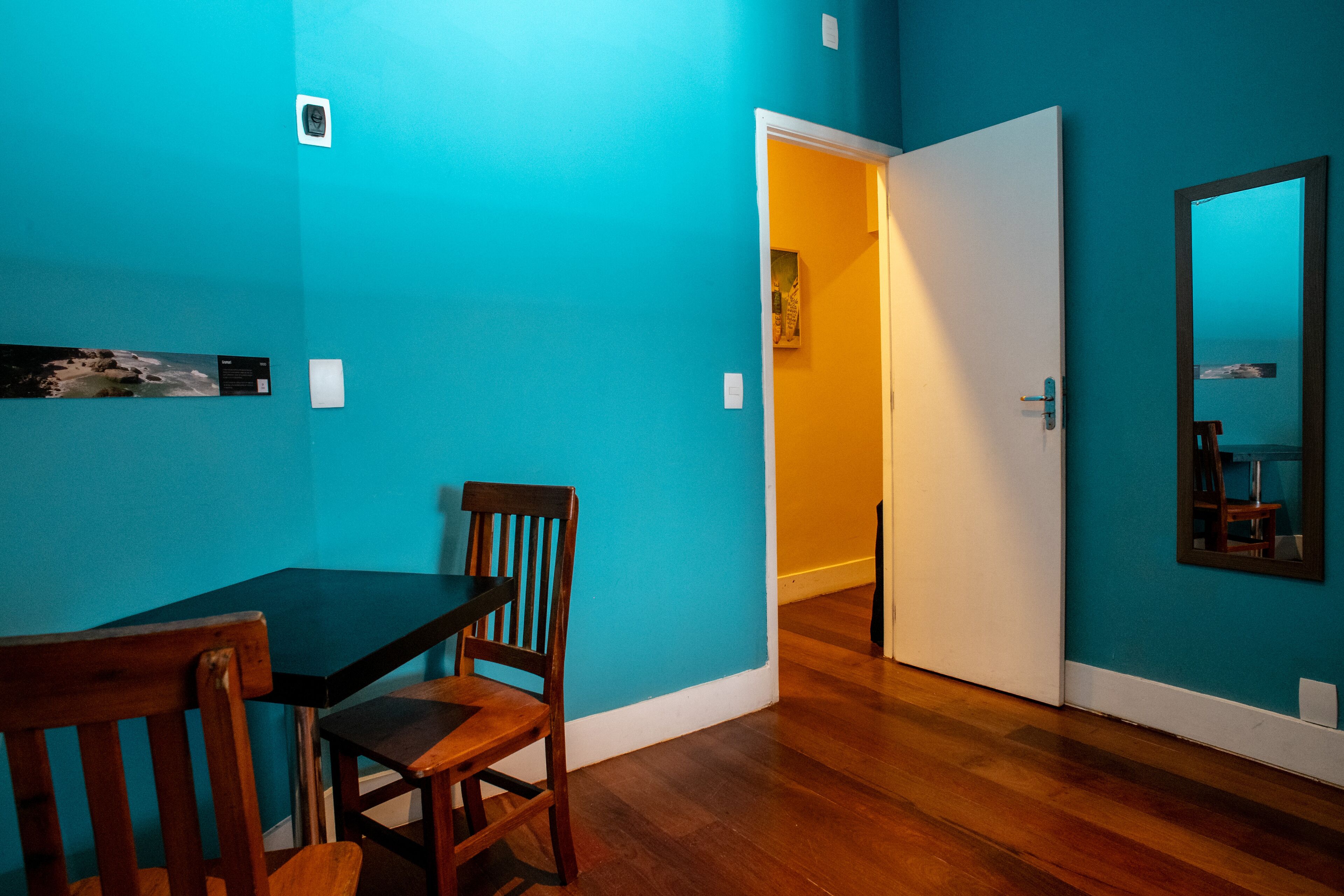 Una habitación con paredes verde azulado, una mesa de comedor de madera con sillas, una puerta blanca y un espejo en la pared.