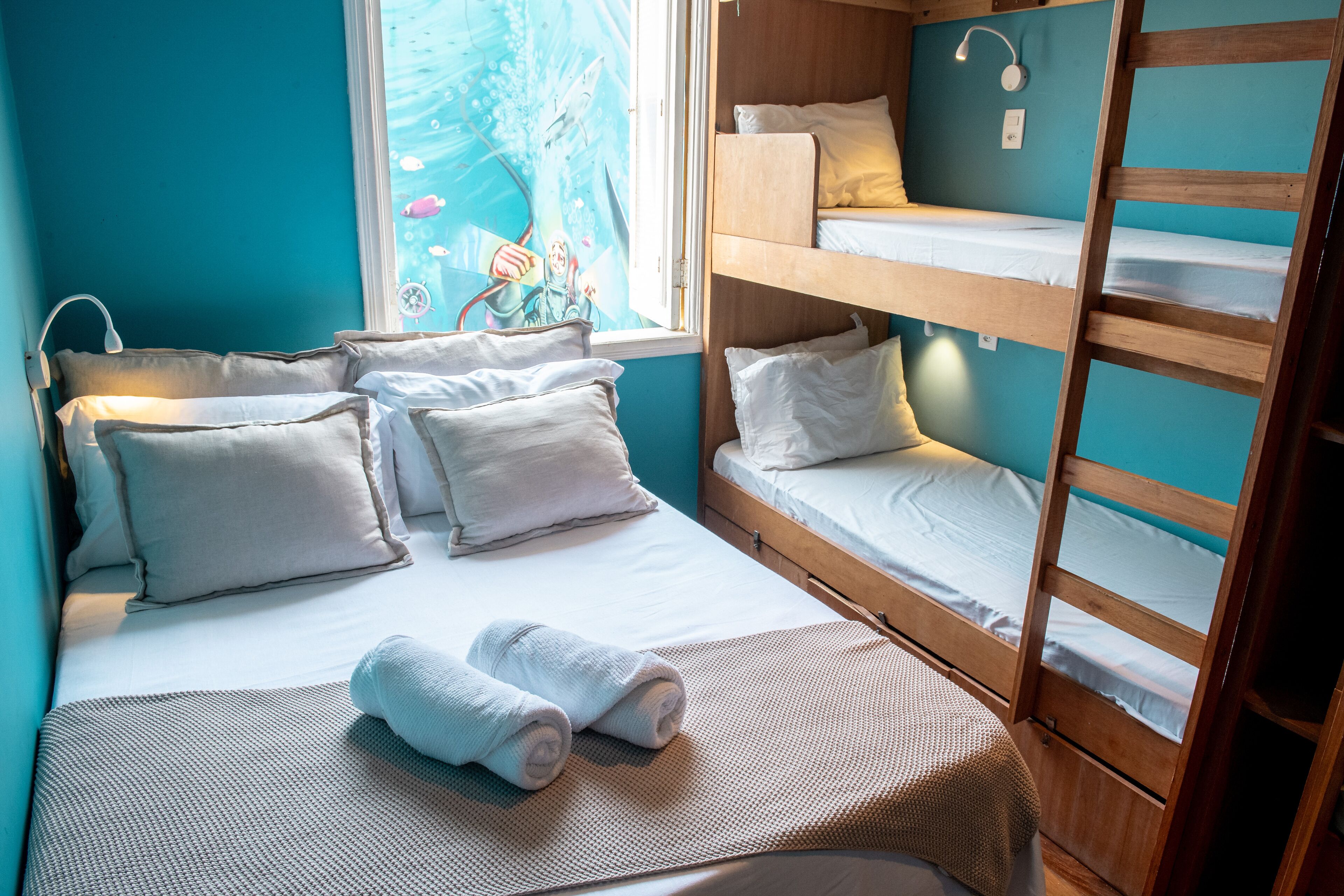 A room with a bunk bed, a single bed, and a window with a view of a cartoon character.
