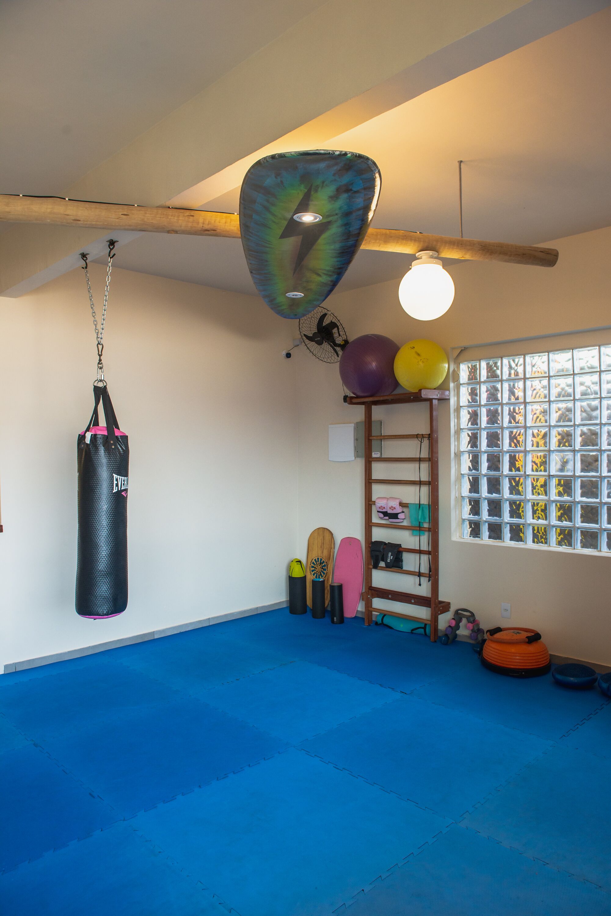 A gym with blue mats, a punching bag, exercise balls, and a wooden beam ceiling.