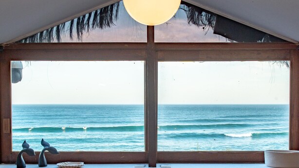 Un área de comedor con una mesa y sillas, una ventana con vista al océano y una lámpara colgante.