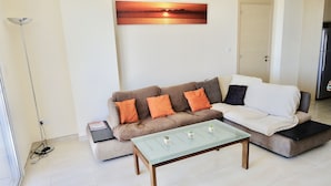 A living room with a sofa, a coffee table, and a painting of a sunset. - Stunning 2-bed Apartment in Poli Crysochous (Polis)