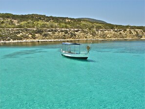 Un bateau nommé « Stellanis » navigue sur une eau turquoise et limpide, avec une côte rocheuse et une végétation luxuriante en arrière-plan.