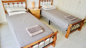 A twin room with two single beds, each with a wooden frame and grey bedding. There is a bedside table with a lamp and a small drawer. - Stunning 2-bed Apartment in Poli Crysochous (Polis)