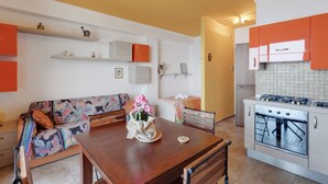 A compact kitchen with a dining area, featuring a wooden table, a sofa, and a built-in oven. - GuestHost - Nice 30sqm studio apartment with breathtaking panoramic sea view, located on the 2nd floor of a building with lift. 10sqm balcony equipped with table, chairs and outdoor furniture to have lunch or enjoy an aperitif while admiring the blue of  (Taormina)