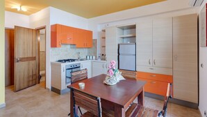A modern kitchen with orange cabinets, a wooden dining table, and a refrigerator. - GuestHost - Nice 30sqm studio apartment with breathtaking panoramic sea view, located on the 2nd floor of a building with lift. 10sqm balcony equipped with table, chairs and outdoor furniture to have lunch or enjoy an aperitif while admiring the blue of  (Taormina)