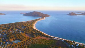 Vue aérienne d’une zone côtière comprenant une plage, une zone boisée et plusieurs petites îles au loin.
