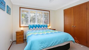 Une chambre à coucher comprenant un lit, des tables de chevet, une fenêtre avec des stores et une armoire en bois.