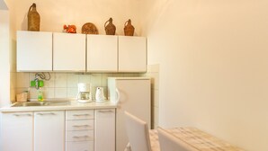 Une cuisine de taille réduite avec des meubles blancs, un évier, une machine à café et un réfrigérateur. Des objets décoratifs sont disposés sur les étagères supérieures.