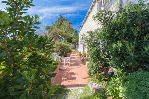 A narrow brick pathway leading to a building with a stone facade, surrounded by lush greenery and potted plants. - Adriatic Star Apartments A 1 (Dubrovnik)