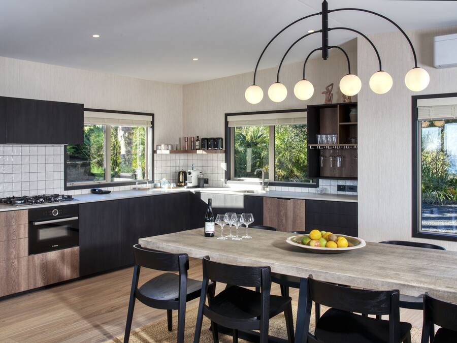 Una cocina moderna con una isla central, armarios oscuros y un ventanal con vistas a zonas verdes.