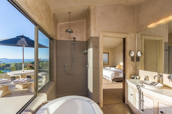 Un bagno moderno con una vasca da bagno ampia, una doccia e un mobile toilette con specchio. Si scorge un balcone con un ombrellone.