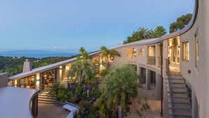 A modern building with a curved roof, outdoor seating, and a staircase leading to a balcony. - Delamore Lodge (Waiheke Island)
