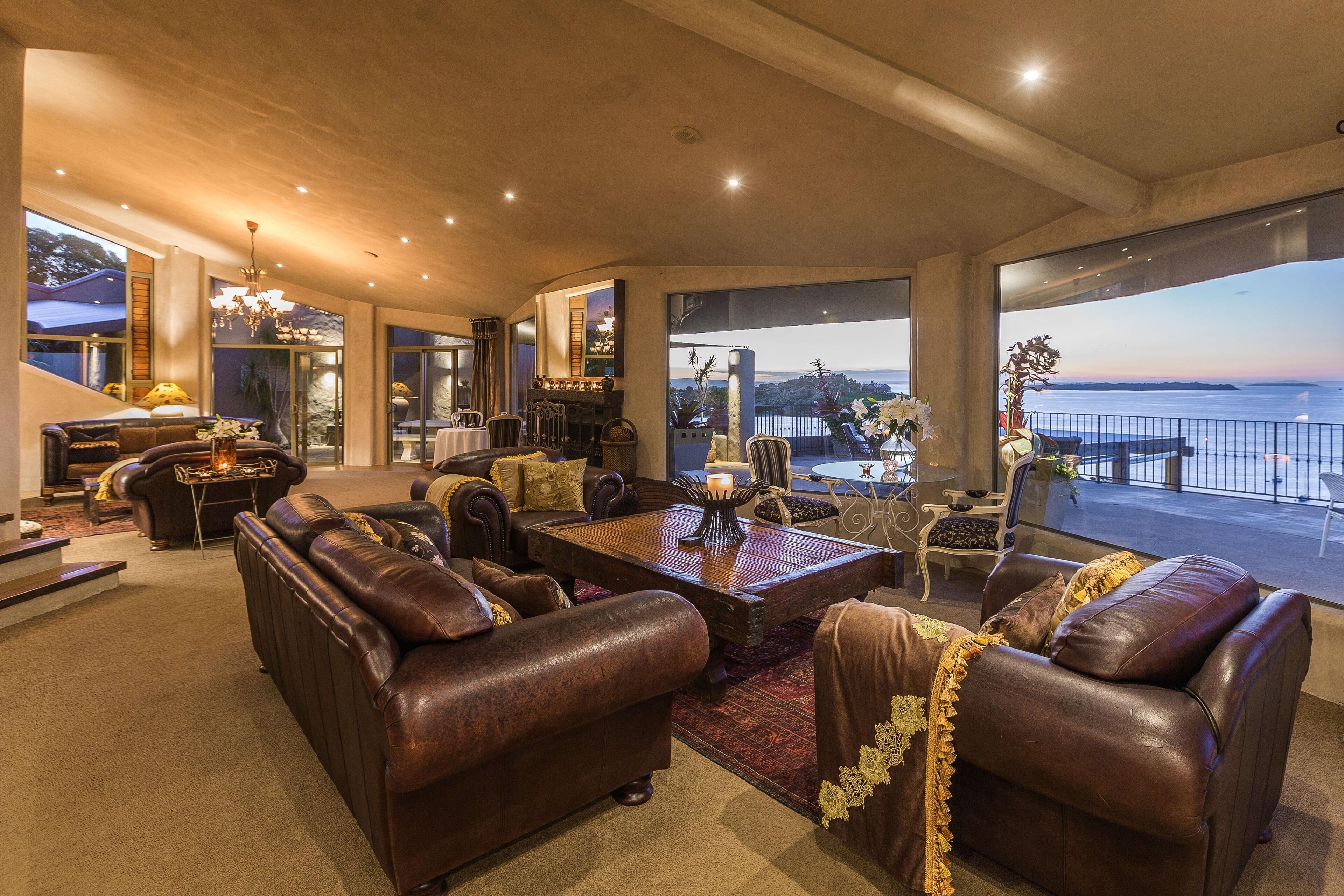 A spacious living room with leather sofas, a wooden coffee table, and a view of the sea.