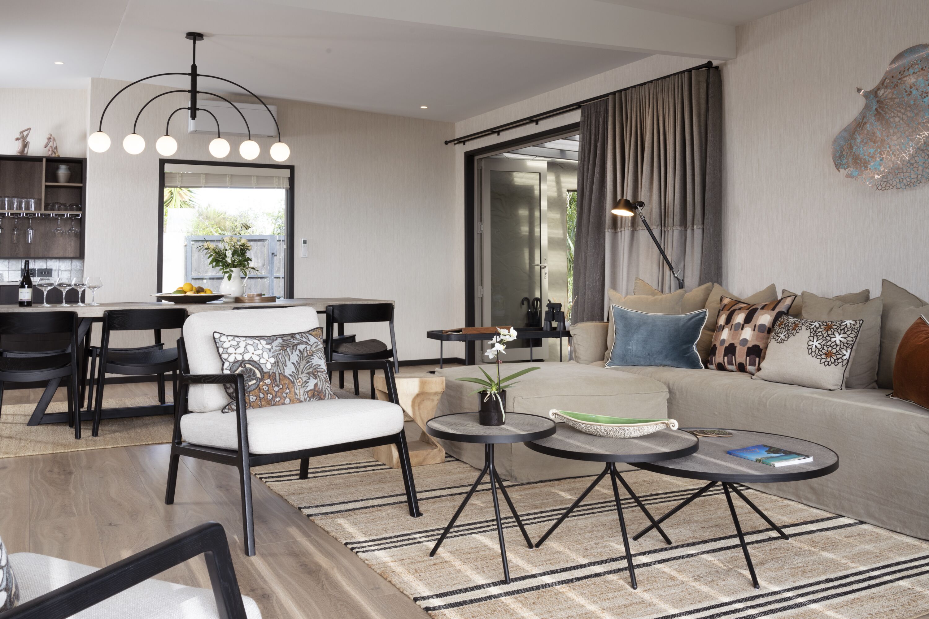 A modern living room with a sofa, two armchairs, a coffee table, and a dining area with chairs and a table.