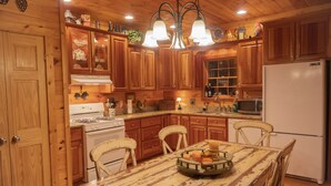 A wooden kitchen with a central island, wooden cabinets, a stove, a refrigerator, and a chandelier. - Smokies Hideaway -  2 bdrms/2 bath, private, SECLUDED, BONFIRE pit, Large driveway (Townsend)