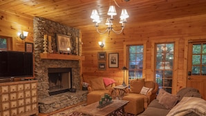 A cozy log cabin interior with a stone fireplace, wooden furniture, and a television. - Smokies Hideaway -  2 bdrms/2 bath, private, SECLUDED, BONFIRE pit, Large driveway (Townsend)