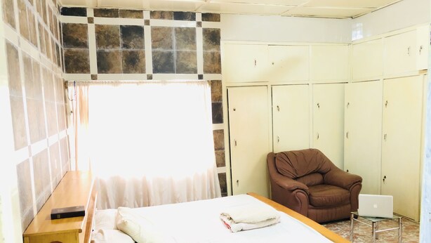 A bedroom with a bed, a chair, a wardrobe, and a small table. - 🌟🧡FREE AIRPORT/BUS TERMINAL TRANSPORTATION (Kumasi)