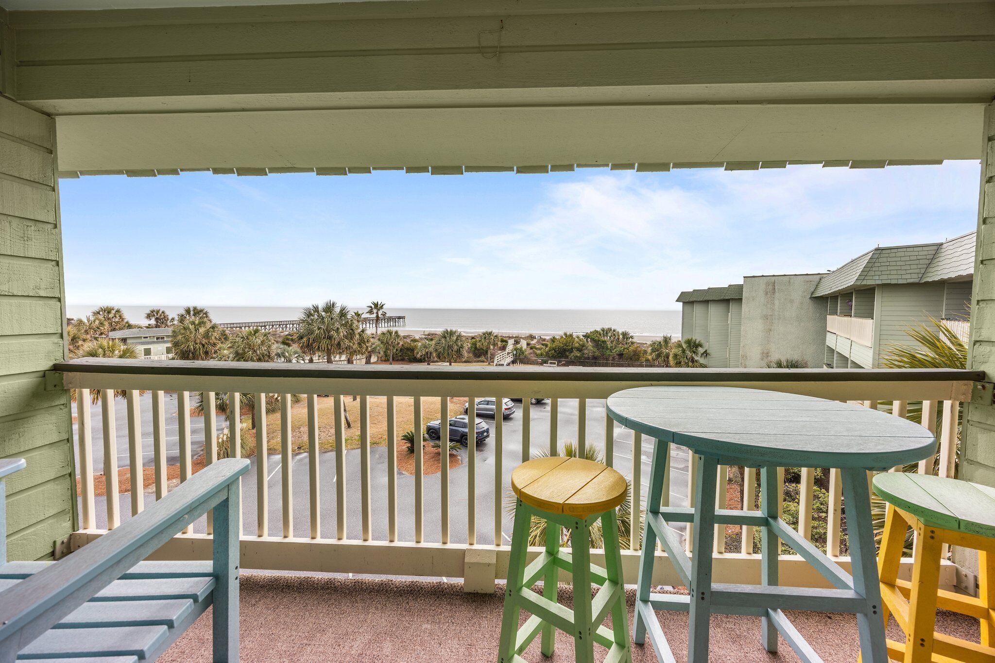 A balcony with a view of the beach, a table, and two stools.