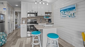 A modern kitchen with white cabinetry, a central island with stools, a microwave, and a painting of a snowy landscape on the wall.